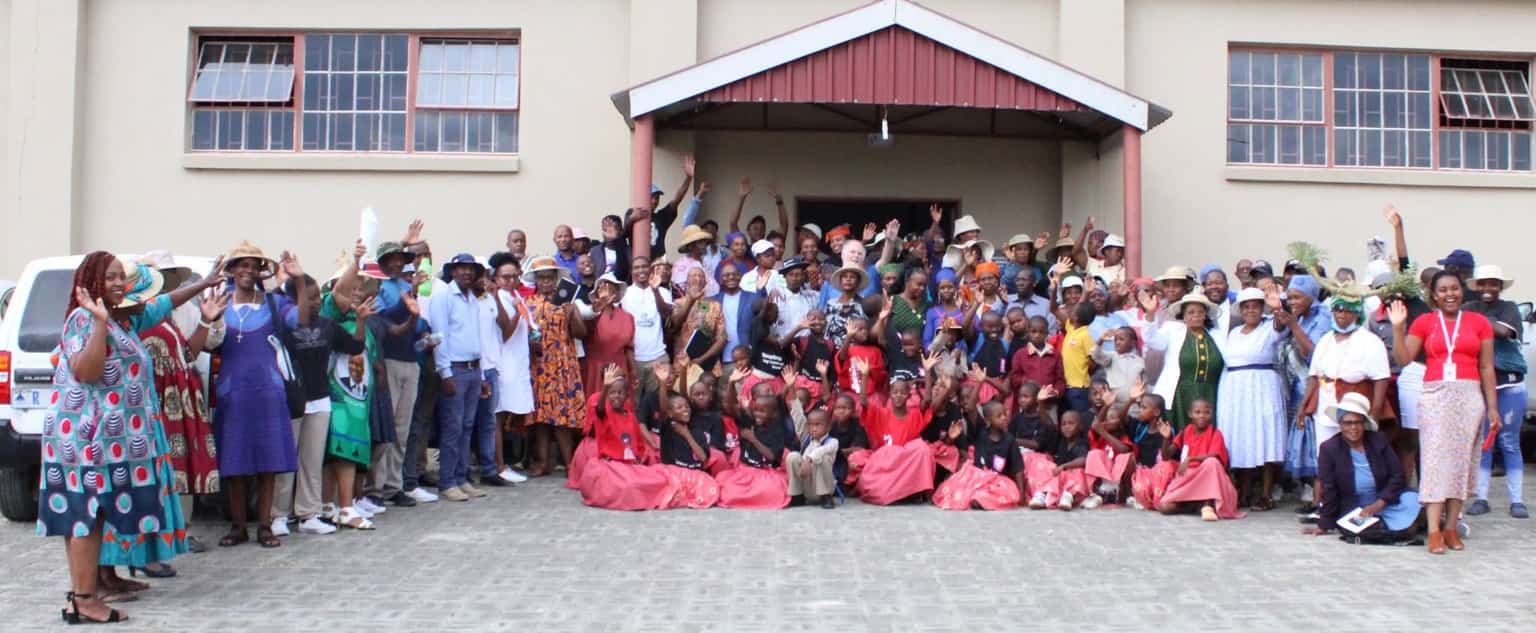 Large community gathering with adults and children waving at camera