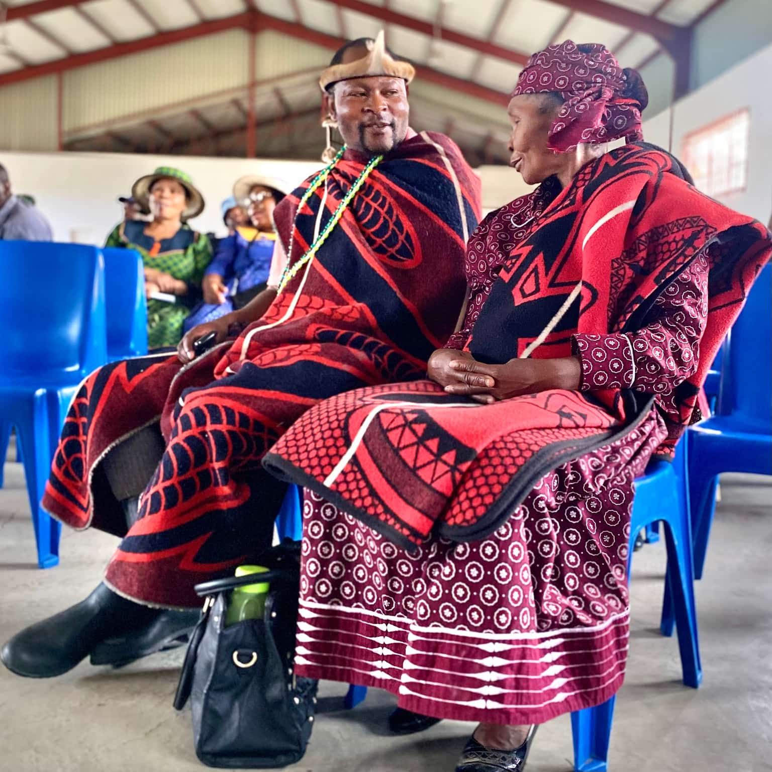 Traditional Basotho couple in ceremonial red and black blankets at a community gathering